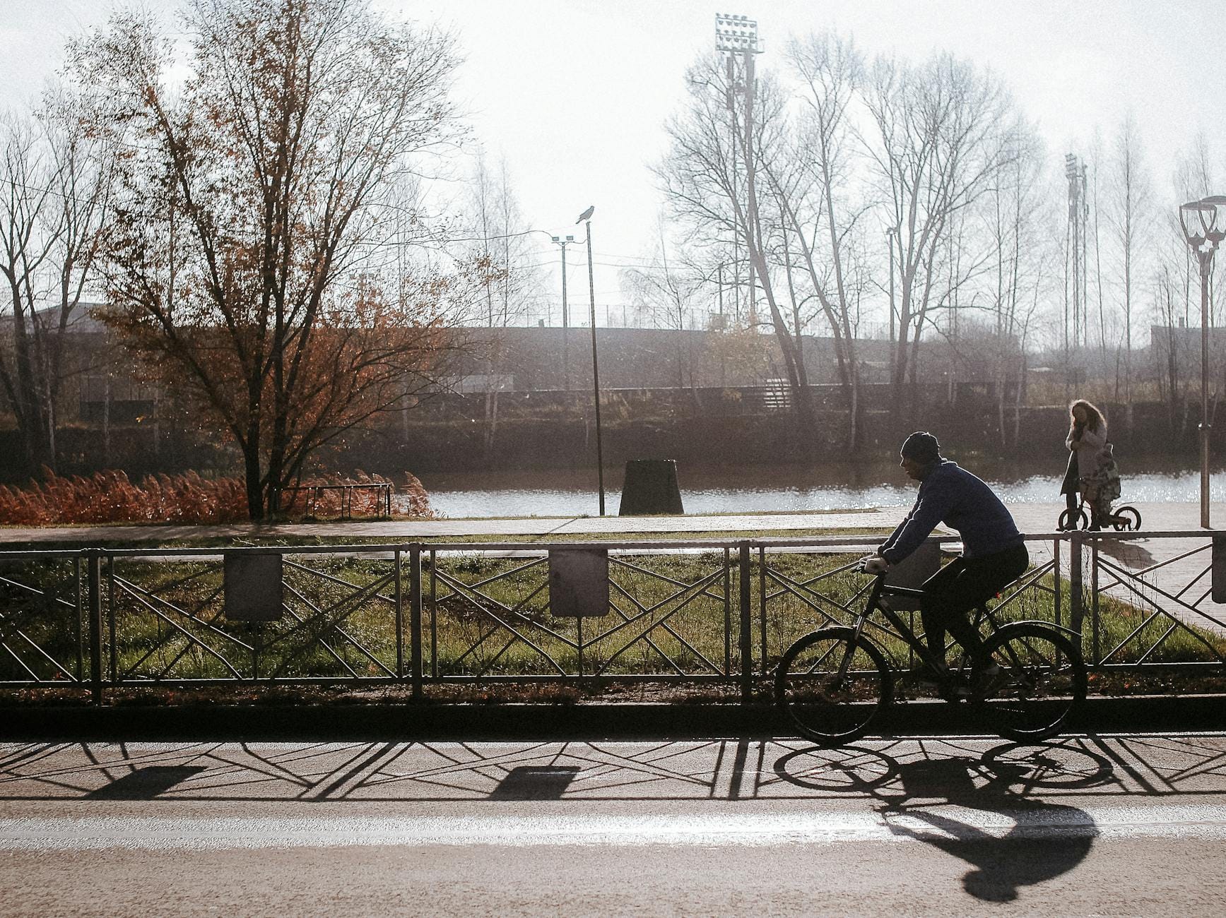 Rowerzysta jedzie ścieżką nad rzeką w słońcu wśród drzew